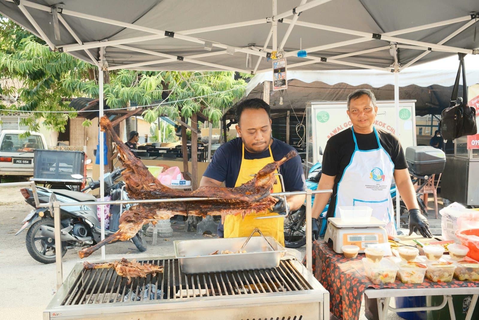 Vendors tending a whole lamb roasting over an open charcoal fire at a Malaysian food stall